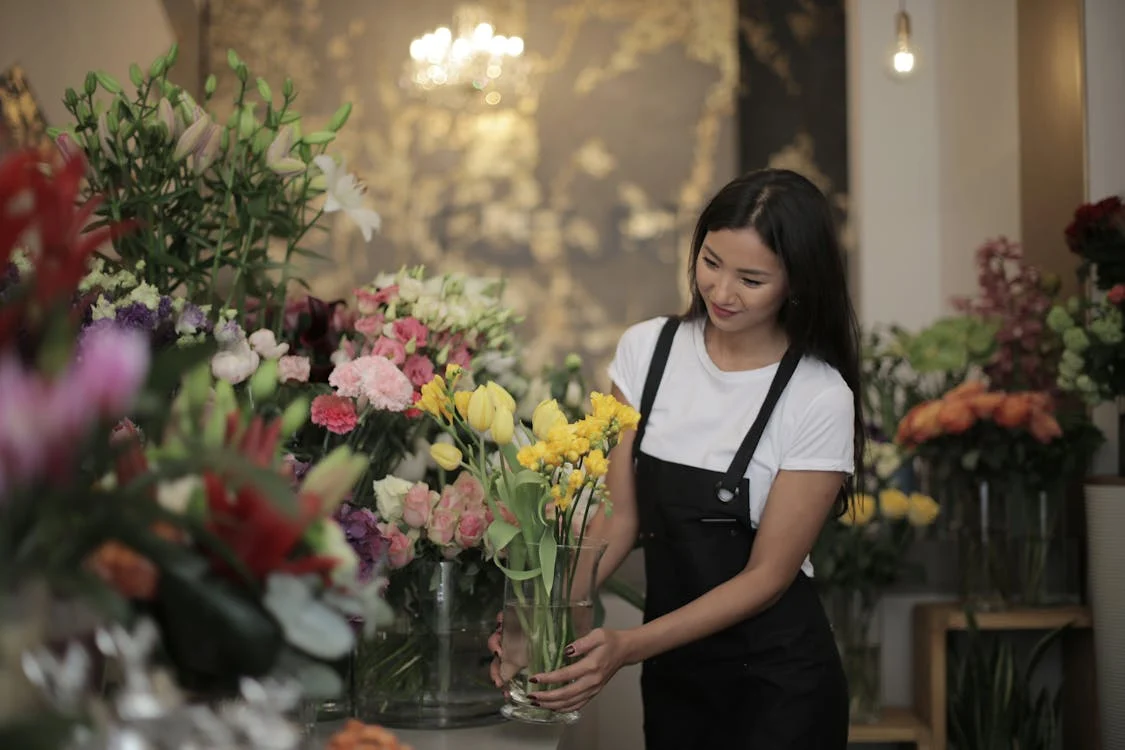 Woman in Black and White Dress Holding Vase with Yellow Flowers